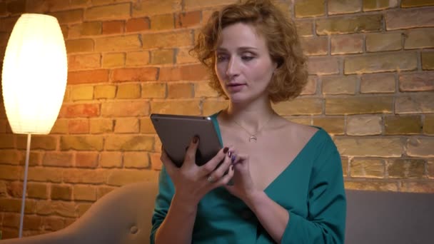 Ginger keriting-rambut gadis Kaukasia mengetik di tablet dan kemudian menunjukkan layar biru itu ke kamera di latar belakang rumah yang nyaman . — Stok Video