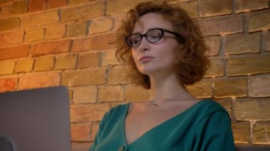 Portre profil zencefil kıvırcık saçlı beyaz kızın gözlüklerini düşünceli laptop ile çalışma kafasına koyar.