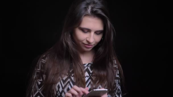 Closeup portret van jonge mooie Kaukasische vrouw met behulp van de telefoon en lachen met geïsoleerd op zwarte achtergrond — Stockvideo