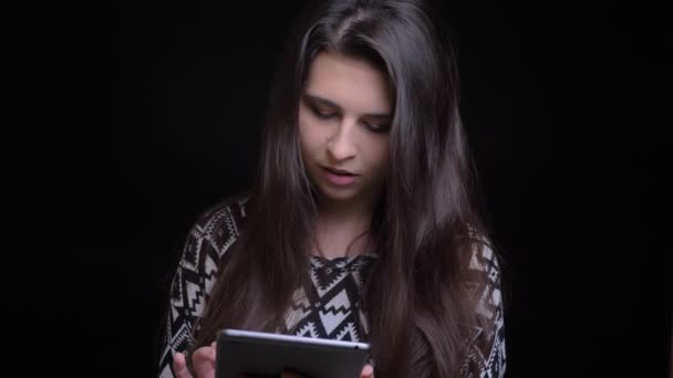 Крупним планом знімок молодих досить кавказьких жіночих смс на планшеті, а потім дивиться на камеру і посміхається з фоном ізольовані на чорному — стокове відео