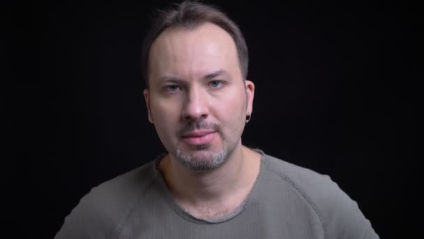 Retrato de hombre caucásico concentrado de mediana edad con pendiente mirando seriamente en la cámara sobre fondo negro . — Vídeos de Stock