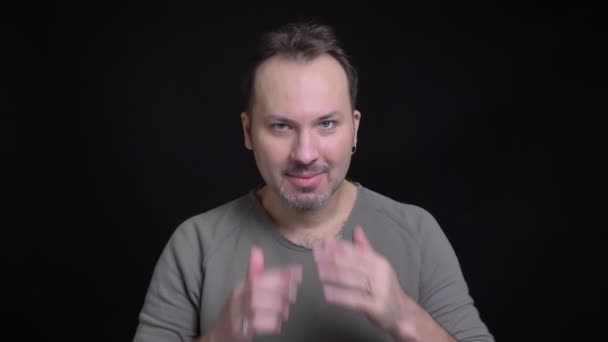 Προσωπογραφία μεσήλικα Καυκάσιος με σκουλαρίκι προσαρμόζει τα μαλλιά του και απλώνεται ένα χέρι για να χαιρετήσει τα φωτογραφικών μηχανών σε μαύρο φόντο. — Αρχείο Βίντεο