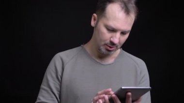 Portresi orta yaşlı beyaz adam cidden tablet siyah arka plan üzerinde içine izlerken Küpeli konsantre.