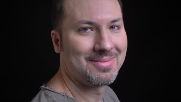 Portrait of middle-aged caucasian man with earring turns to camera and watches happily into camera on black background. — Stock Video