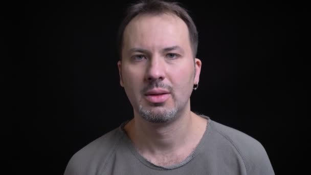 Портрет белого мужчины средних лет с серьгой, смотрящей в камеру с замешательством на черном фоне . — стоковое видео