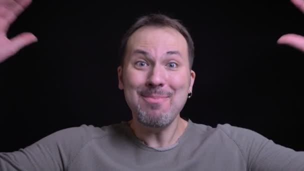 Portrait of middle-aged caucasian man with earring watching extremely happily into camera on black background. — Stock Video