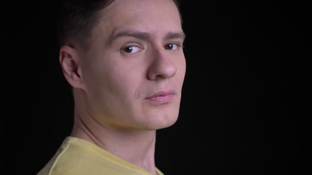 Close-up portrait in profile of middle-aged concentrated caucasian man in yellow sweater watching seriously into camera on black background. — Stock Video