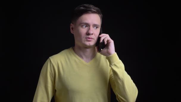 Portret kaukaski mężczyzna w średnim wieku w żółty sweterek rozmawia uważnie smartphone na czarnym tle. — Wideo stockowe