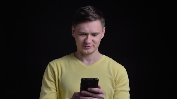 Portret kaukaski mężczyzna w średnim wieku w żółty sweterek rozmawia w videochat szczęśliwie smartphone na czarnym tle. — Wideo stockowe