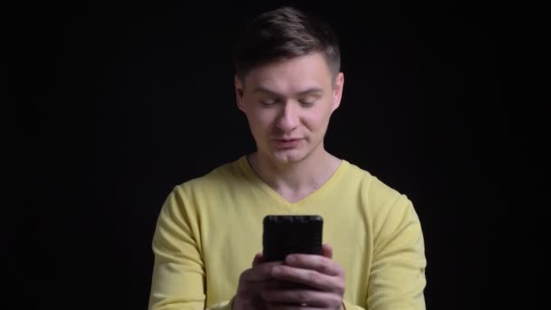 Mosolyogva beszél videochat boldogan okostelefon fekete háttér sárga pulóver-középkorú kaukázusi Férfi portréja. — Stock videók