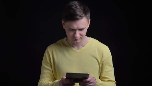 Портрет белого мужчины средних лет в желтом свитере, улыбающегося в планшет на черном фоне . — стоковое видео