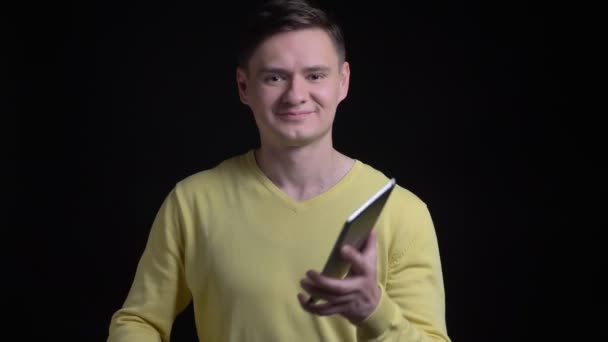 Hombre caucásico de mediana edad en suéter amarillo que muestra la pantalla azul de la tableta felizmente en la cámara sobre fondo negro . — Vídeo de stock