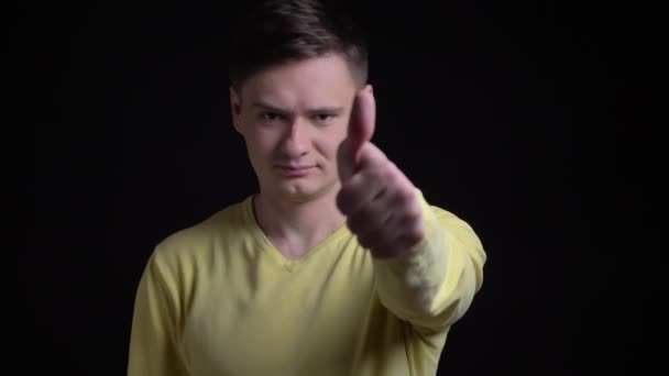 Hombre caucásico de mediana edad en suéter amarillo haciendo gestos con los dedos hacia arriba para mostrar como y respetar en la cámara en el fondo negro . — Vídeos de Stock