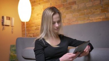 Portre portre genç güzel sarışın kadın katta oturan o zaman rahat ev kapalı kameraya bakarak tablet kullanma