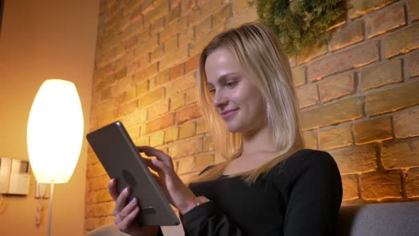 Closeup vista lateral retrato de jovem dona de casa bonita usando o tablet e sentado no sofá dentro de casa aconchegante — Vídeo de Stock