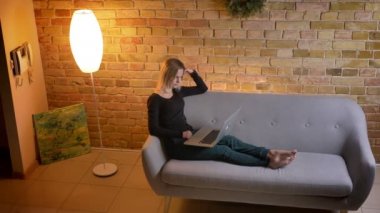 Yan görünüm portre rahat ev kapalı, kanepede otururken dizüstü bilgisayarda tarama genç güzel kadın genç