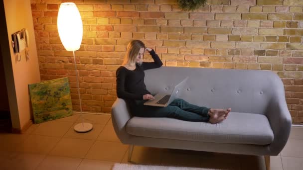 Side view porträtt av unga ganska kvinnliga tonåringen surfing web på den bärbara datorn medan du sitter i soffan inomhus på mysiga hem — Stockvideo