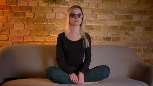 Closeup schieten van het jonge mooie blonde vrouw kijken naar een 3d film op Tv zittend op de Bank binnen in een gezellig appartement — Stockvideo