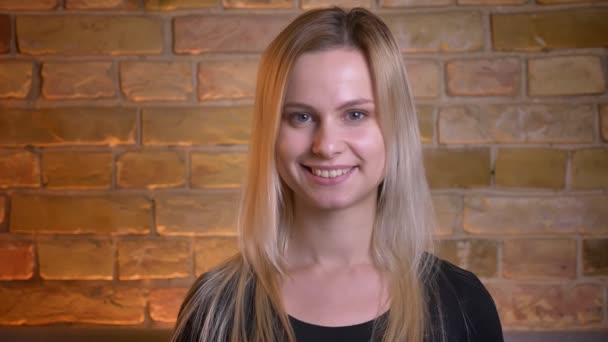 Nahaufnahme Porträt einer jungen hübschen blondhaarigen Frau, die direkt in die Kamera schaut und zu Hause glücklich lächelt — Stockvideo