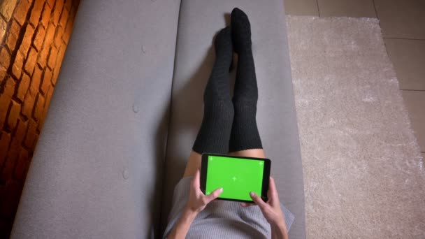 Closeup tiro de pernas femininas em meias bonitos no sofá dentro de casa. Mulher mensagens de texto e bate-papo no tablet com tela de croma verde — Vídeo de Stock