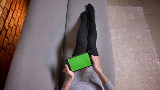 Closeup tiro de pernas femininas em meias bonitos no sofá dentro de casa. Mulher jogando jogos de vídeo no tablet com tela de croma verde — Vídeo de Stock