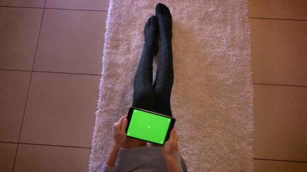 Closeup πυροβολούν νεαρό θηλυκό έφηβος παιχνίδια βίντεο στο tablet με πράσινη οθόνη. Κορίτσια τα πόδια σε χαριτωμένο κάλτσες στο χαλί σε εσωτερικούς χώρους — Αρχείο Βίντεο