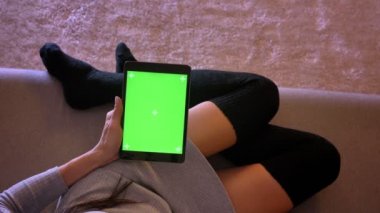 Genç güzel kadın ağ tablet yeşil ekran ile portre portre. Çorap kanepede rahat bir pozisyonda bacaklarda kızlar