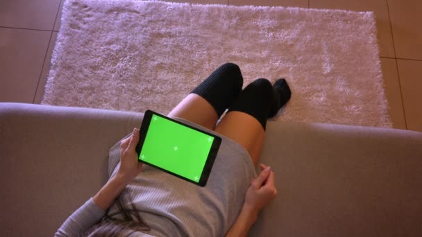 Sesión de primer plano de la joven adolescente jugando video en la tableta con pantalla verde verticalmente. Chicas piernas en calcetines lindos sentados en el sofá en el interior — Vídeo de stock