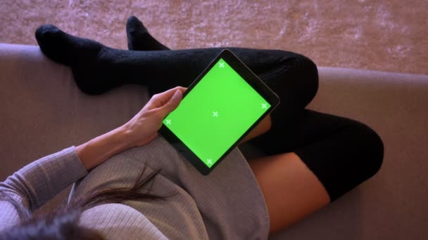 Крупный план портрета молодой красивой женщины, играющей видео на планшете с зеленым экраном. Девочки ноги в уютном положении в носках на диване — стоковое видео