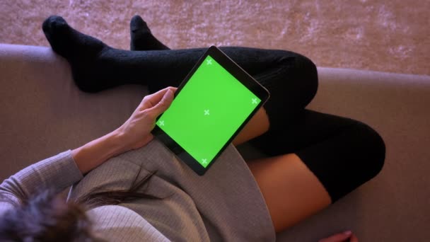 Retrato de primer plano de la joven bonita hembra navegando en la tableta con pantalla verde. Las niñas piernas en una posición acogedora en calcetines en el sofá — Vídeo de stock