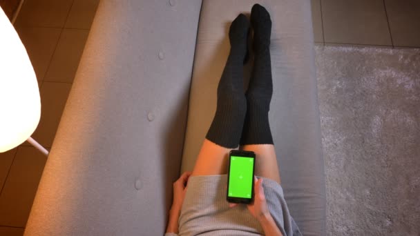 Primeros planos de joven atractiva hembra viendo un video usando el teléfono con pantalla verde. Mujeres piernas en calcetines lindos en el sofá — Vídeos de Stock