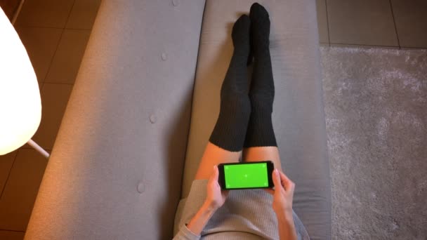 特写镜头拍摄的年轻少女拿着手机与绿色屏幕上的广告。女孩腿在可爱的袜子在沙发上 — 图库视频影像