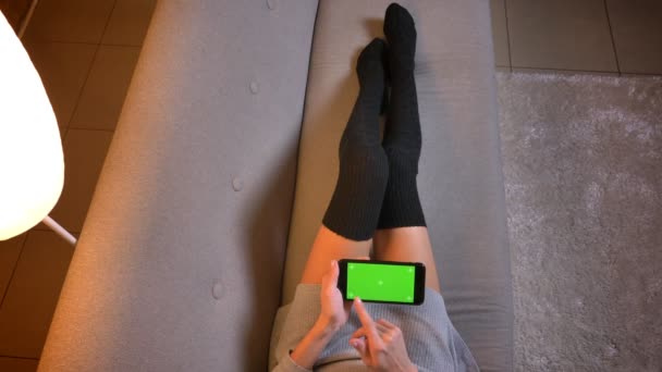 美しい十代の若者に緑色の画面で携帯電話を使用している間オンライン ショッピングのクローズ アップ撮影。ソファの上のかわいい靴下で梨花の足 — ストック動画