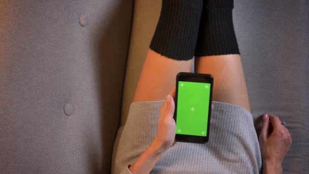 Крупный план съемки молодой сексуальной женщины с помощью телефона с зеленым экраном. Женские бёдра в соблазнительных носках на диване — стоковое видео