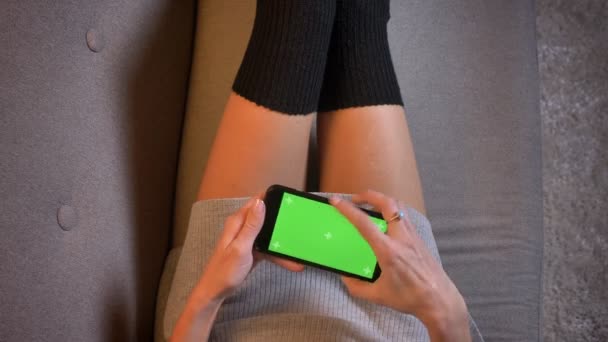Крупним планом знімок молодої сексуальної жіночої тисячоліття отримує сповіщення і повідомлення по телефону з зеленим екраном. Жінки стегна в спокусливих шкарпетках на дивані — стокове відео