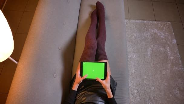 Close-up opnamen van vrouwelijke sociale media beïnvloeder texting op de tablet met groene chroma scherm. Dames dijen in leuke gebreide sokken en lederen rok op de Bank — Stockvideo