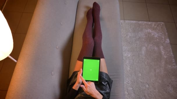 Gros plan shoot de blogueuse de médias sociaux achats en ligne sur la tablette avec écran chromatique vert. Cuisse de fille en mignon tricot chaussettes et jupe en cuir sur le canapé — Video