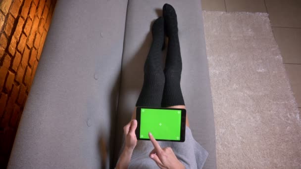 Closeup tiro de pernas femininas em meias bonitos no sofá dentro de casa. Mulher segurando o tablet com tela verde horizontalmente e rolando — Vídeo de Stock