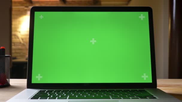 Съемка крупным планом с помощью камеры перемещается от ноутбука с зеленым экраном на столе к виду сотрудника на заднем плане в помещении офиса — стоковое видео