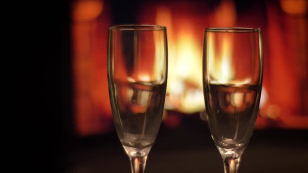 Closeup shoot of two empty wine glasses with cozy warm fireplace with flames on the background indoors in a dark apartment — Stock Video