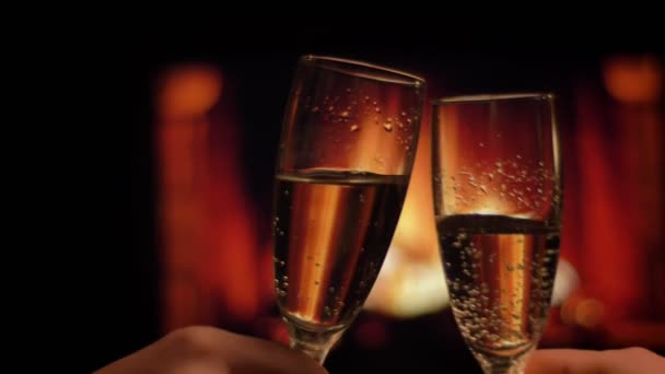 Крупним планом зйомка двох рук друзів клінкерні окуляри, повні шампанського охолодження ввечері з затишним теплим каміном на фоні в приміщенні — стокове відео