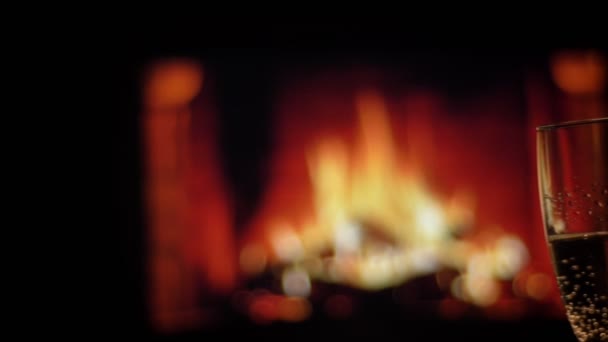 Closeup shoot of two hands of friends clinking glasses full of champagne chilling indoors with cozy warm fireplace on the background — Stock Video