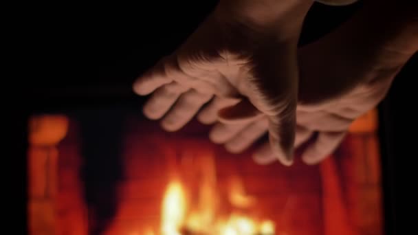 Крупним планом знімок чоловічих рук, що натираються і зігріваються перед затишним гарячим каміном і горінням деревини в холодну зимову пору року в приміщенні — стокове відео