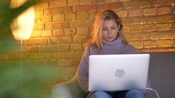 Zbliżenie strzelać dorosły kaukaski blond kobiece pisanie na laptopie siedząc na kanapie pomieszczeniu w przytulnym domu — Wideo stockowe