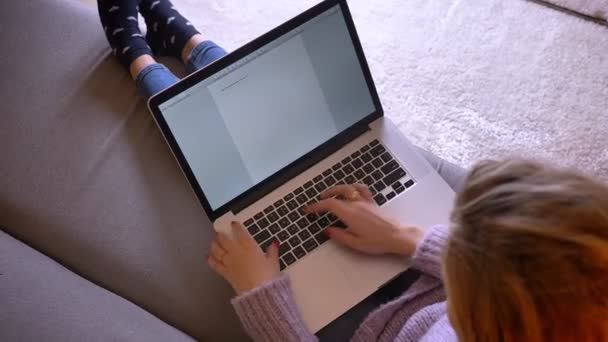 Задний план Съемка взрослой белой привлекательной женщины, печатающей на ноутбуке и пишущей эссе, сидя на диване в помещении — стоковое видео