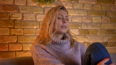 Closeup çekim yetişkin beyaz sarışın kadın kapalı couh üzerinde otururken dokundu ve melankolik olmak Tv izlerken