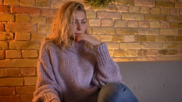 Съемки крупным планом взрослой кавказской блондинки, смотрящей телевизор, трогательный и грустный плач, сидя на диване в уютном доме — стоковое видео
