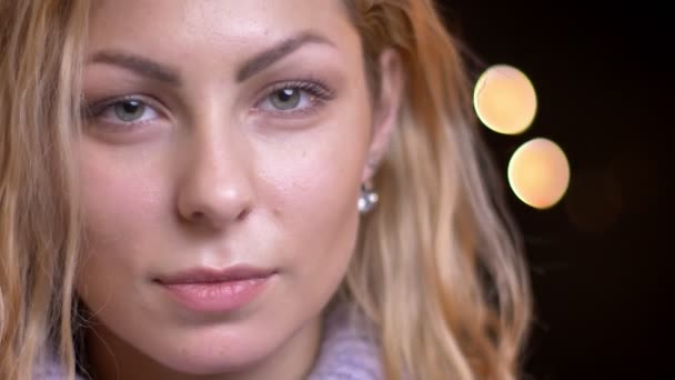 Close-up tiro de adulto atraente loira caucasiano fêmea olhando em linha reta para a câmera com bokeh luzes no fundo — Vídeo de Stock
