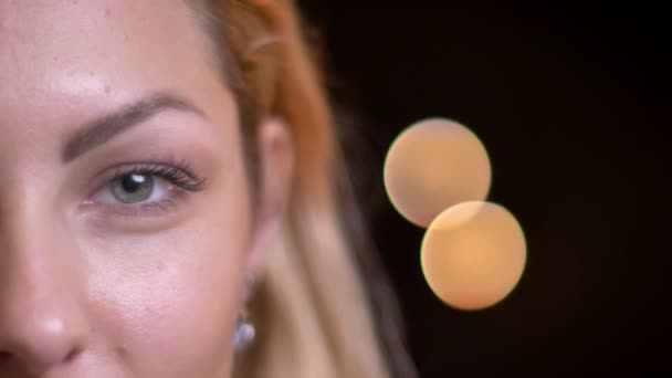 Closeup half-face portret van volwassen aantrekkelijke blonde Kaukasische vrouwelijke kijken rechtdoor camera met bokeh achtergrond — Stockvideo