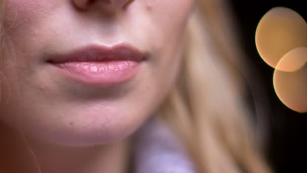 Съемки крупным планом взрослых привлекательных белокурых кавказских женских губ, соблазнительно улыбающихся боке-огнями на заднем плане — стоковое видео